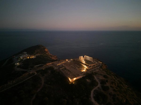 Night view of the Temple of Poseidon at Cape Sounion illuminated, with the sea and sky at sunset in the background.