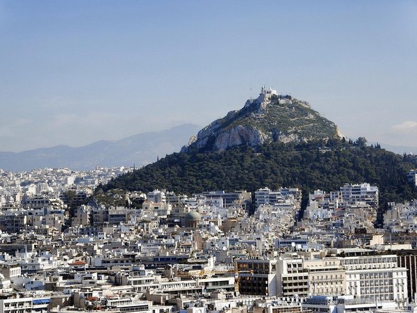 Panoramic view of Athens with Mount Lycabettus in the background, an iconic green hill topped with a chapel.