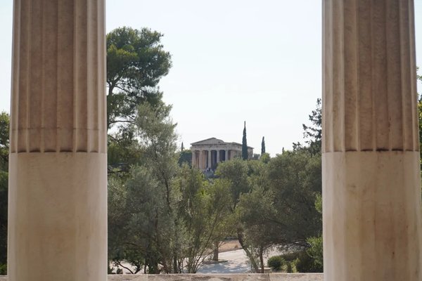 View of an ancient Greek temple through columns, surrounded by trees and vegetation in Athens.