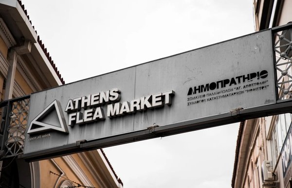 Sign of the Athens flea market with English and Greek writing, cloudy sky in the background.