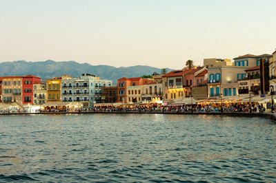 Panoramic view of the Venetian harbor of Chania in Crete at sunset, with colorful buildings and mountains in the background.