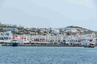 Panoramic view of Mykonos with white buildings, blue domes, and boats along the waterfront.