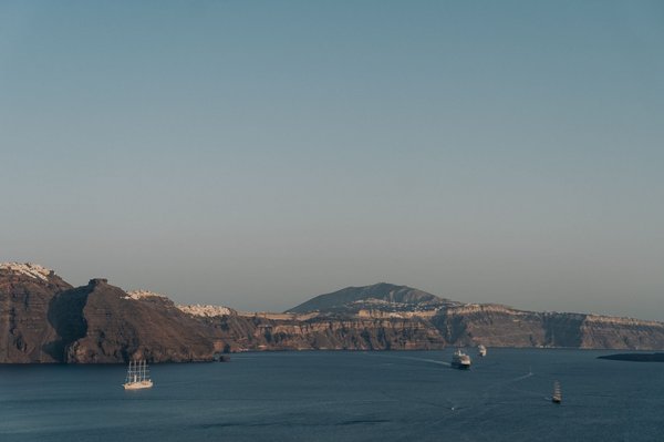 Boats crossing the caldera toward the dark volcanic islets where Santorini's hot springs excursions depart from.