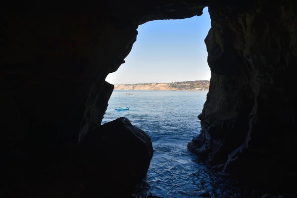 View through a sea cave entrance with kayaks floating on the water outside.