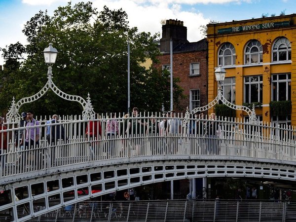 Ha'penny Bridge in Dublin with pedestrians and colorful buildings in the background.
