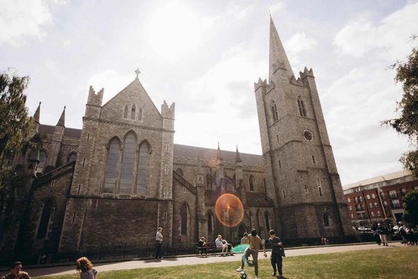 St. Patrick's Cathedral in Dublin with people relaxing in the surrounding park on a sunny day.