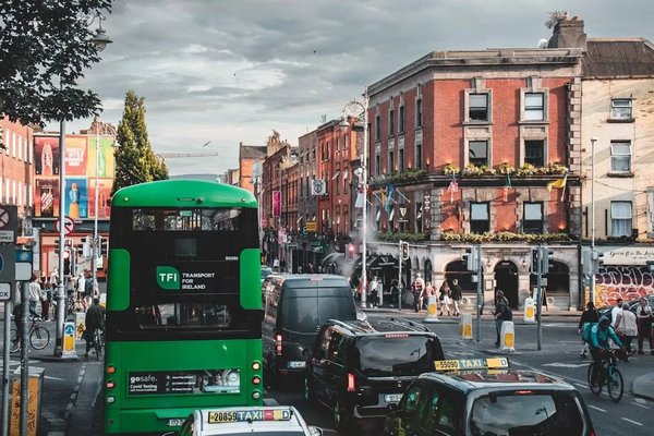 Dublin street with green TFI bus, red brick buildings, and lively atmosphere.