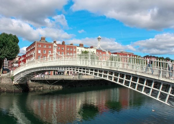 Ha'penny Bridge in Dublin with historic buildings in the background and reflections in the water.