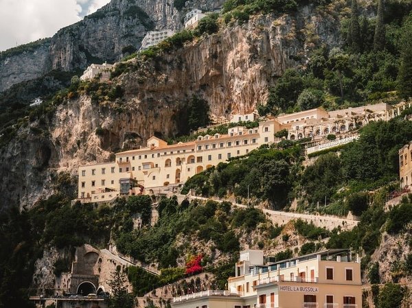 View of cliffside buildings on the Amalfi Coast with lush greenery and a clear sky.