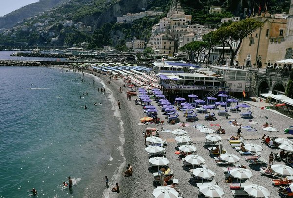 Marina Grande Beach in Amalfi with colorful umbrellas, beachgoers, and a view of coastal houses.