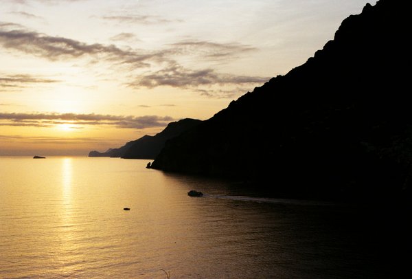 Sunset over the Amalfi Coast with cliffs and a boat on calm waters.