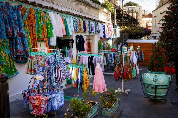 Local market in Amalfi with colorful clothing, bags, and vibrant decorations displayed outdoors.
