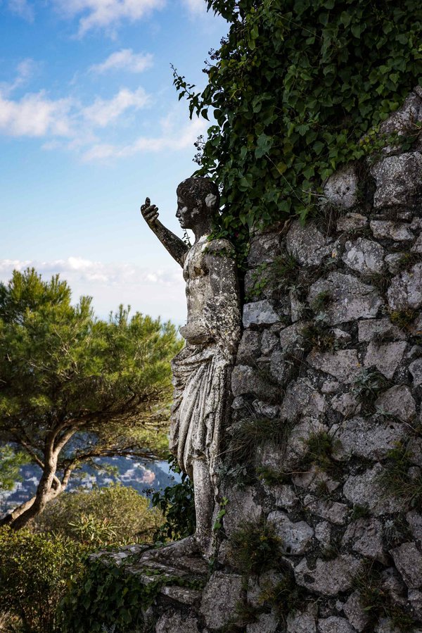 Ancient statue in the Gardens of Augustus in Capri, surrounded by greenery and blue sky.