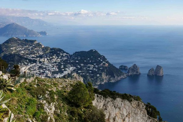 Panoramic view of Capri and the Faraglioni from Monte Solaro, with blue sea and lush vegetation.