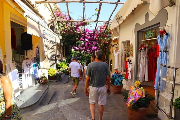 Via Camerelle in Capri with boutique shops, colorful flowers, and people strolling.