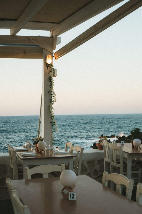 Seaside terrace at sunset with set dining tables, ocean view, and floral decorations.