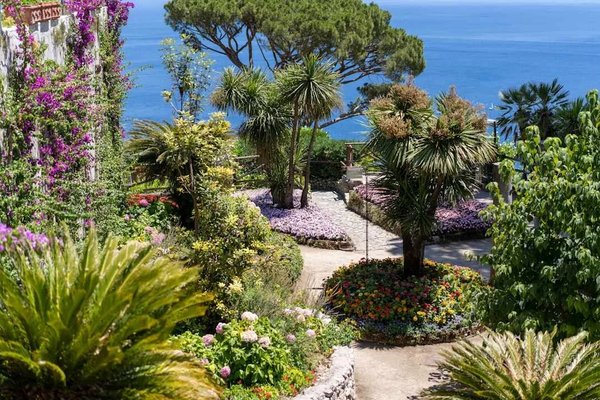 Gardens of Villa Lysis in Capri with colorful flowers, trees, and a view of the blue sea.
