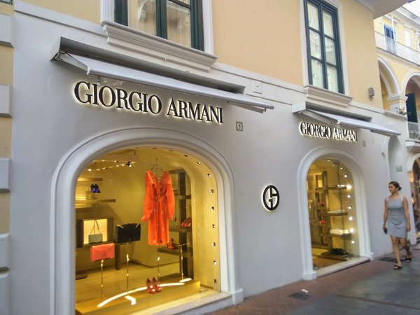 Boutique Giorgio Armani su Via Camerelle a Capri con vetrine illuminate e abiti di lusso in esposizione.