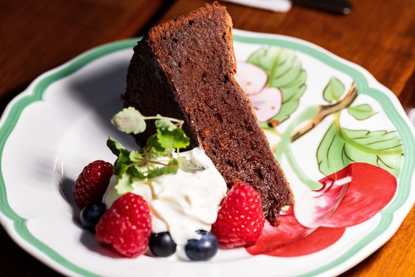 Fetta di torta al cioccolato con frutti di bosco e panna su un piatto decorato.