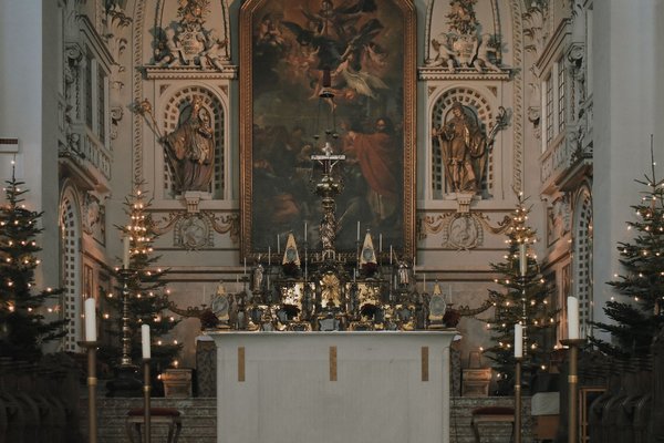 An ornate Baroque church altar decorated with Christmas trees and candlelight.