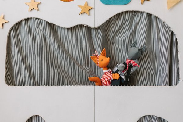 Un pupazzo volpe e un pupazzo lupo si esibiscono insieme su un palco colorato per marionette.