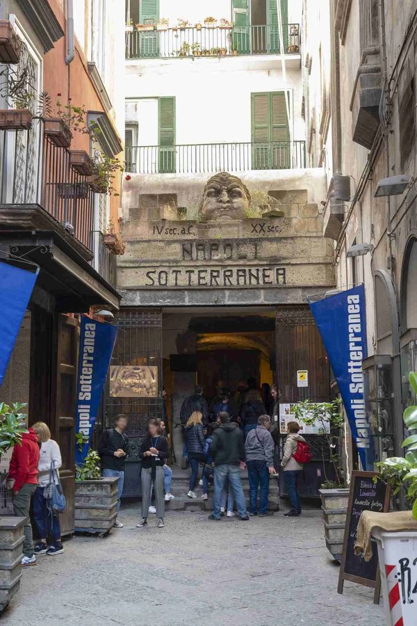 Ingresso di Napoli Sotterranea con visitatori e insegne blu, un'attrazione iconica del sottosuolo di Napoli.