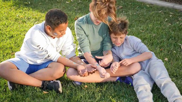 Bambini seduti sull'erba in un parco, con tatuaggi temporanei sulle braccia.