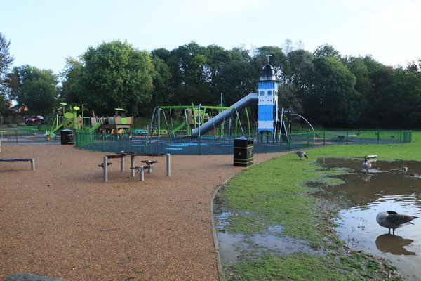 Un parco giochi colorato con uno scivolo a torre vicino a uno stagno frequentato dalle anatre.