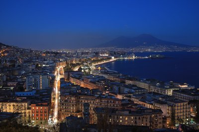 Night view of Naples with Mount Vesuvius in the background and the illuminated coastline.