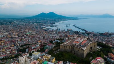 Vista panoramica di Napoli con Castel Sant'Elmo, il Vesuvio e il Golfo di Napoli sullo sfondo.