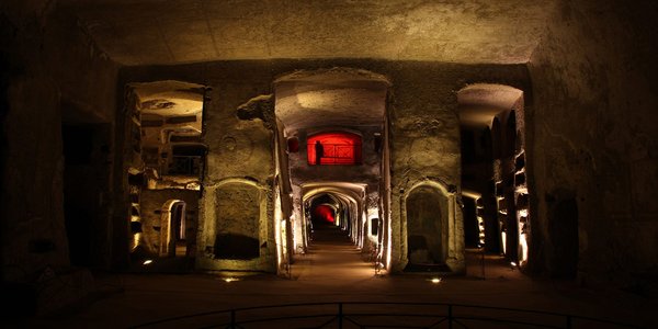 Interno delle Catacombe di San Gennaro a Napoli, con illuminazione drammatica e architettura sotterranea.