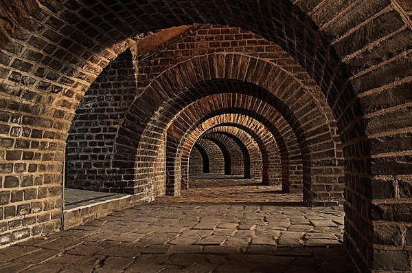 Una galleria in mattoni a volta che si perde nell'oscurita, evocando i passaggi sotterranei della Galleria Borbonica.
