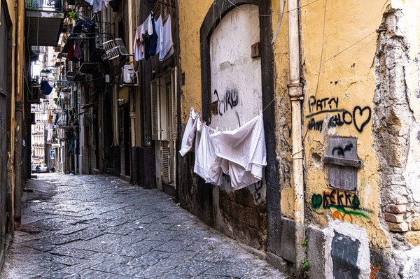 Una stretta strada storica di Napoli fiancheggiata da facciate sbiadite e biancheria stesa tra i balconi.