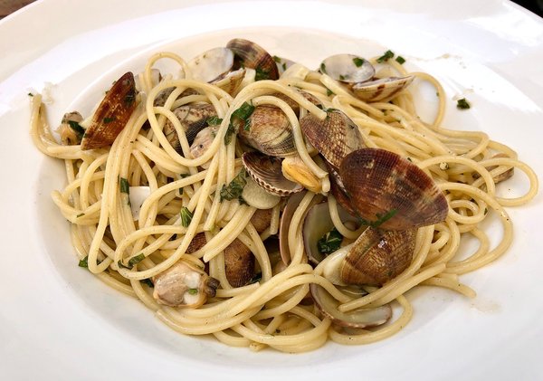 Spaghetti with clams served on a white plate, a traditional dish of Neapolitan cuisine.