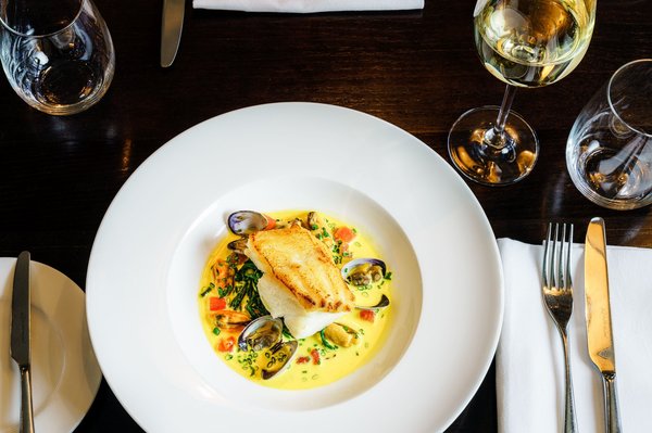 Elegant seared fish fillet with clams and mussels in a delicate broth, fine dining presentation.