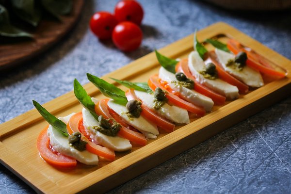 Buffalo mozzarella with tomatoes, basil, and pesto on a wooden plate, a staple of Neapolitan cuisine.