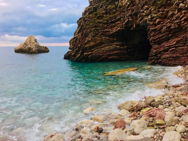 Crystal-clear turquoise water lapping a pebble beach beside dramatic Amalfi Coast cliffs.