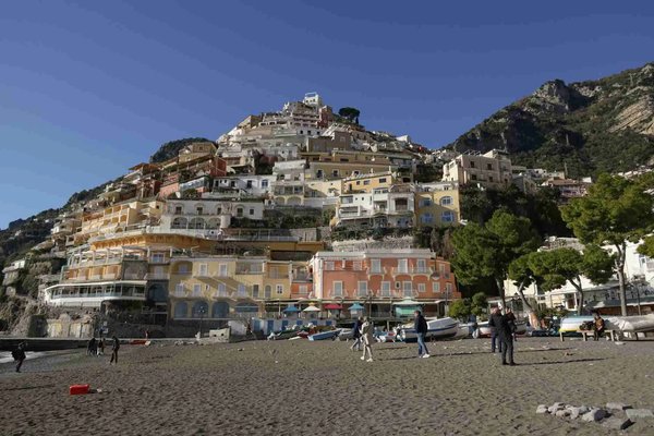 View of Positano's colorful houses from the beach, with clear skies and people strolling.