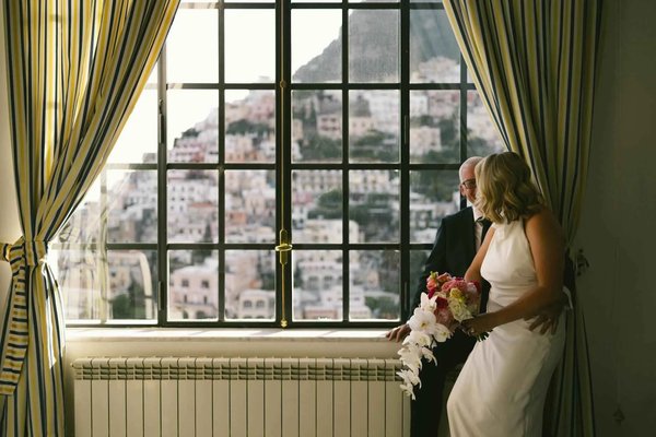 Romantic view of Positano through a window with an elegant couple and a bouquet of flowers.