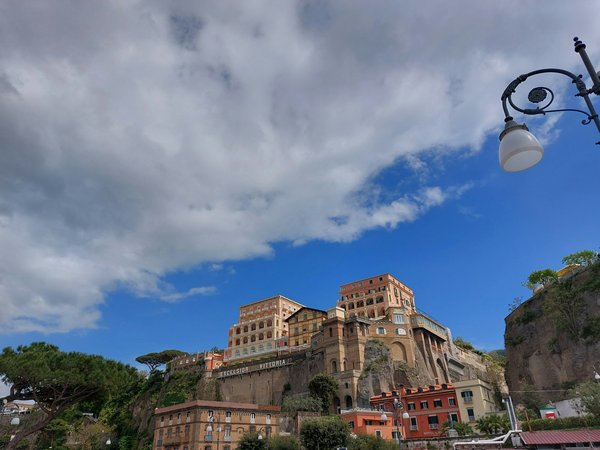 Vista di edifici storici su una scogliera a Sorrento vicino a Piazza Tasso, con cielo blu e nuvole.