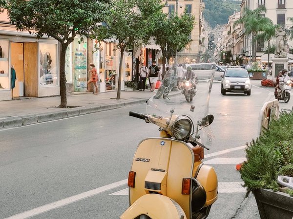 Vespa gialla parcheggiata su Corso Italia a Sorrento, con negozi, alberi e traffico sullo sfondo.