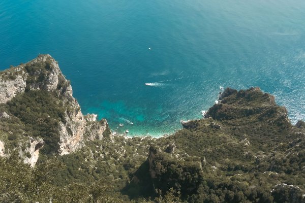 Vista aerea delle scogliere e del mare turchese di Capri, con una barca che solca l'acqua.