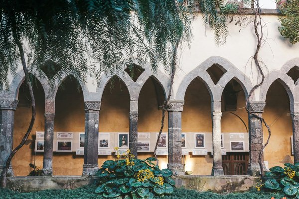 Chiostro di San Francesco a Sorrento con archi gotici, piante verdi e pannelli espositivi.