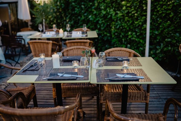 An intimate candlelit restaurant terrace with wicker chairs, set for an evening dinner.