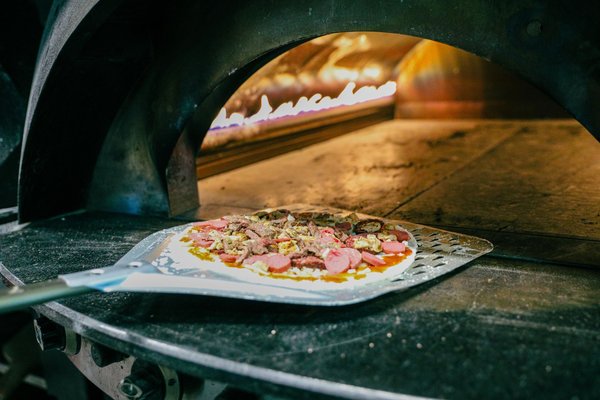 A pizza slides into a glowing wood-fired oven on a floured peel.