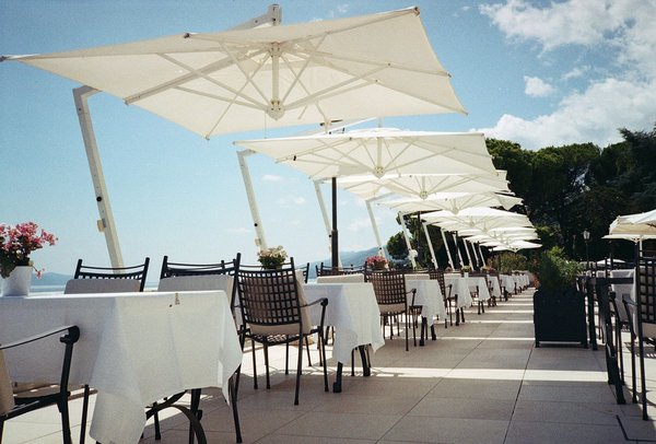 A row of white umbrellas shading linen-set tables on a panoramic seaside terrace.