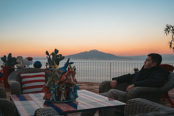 Sunset view with Mount Vesuvius in the background, decorated dining table and chairs in an outdoor setting in Sorrento.