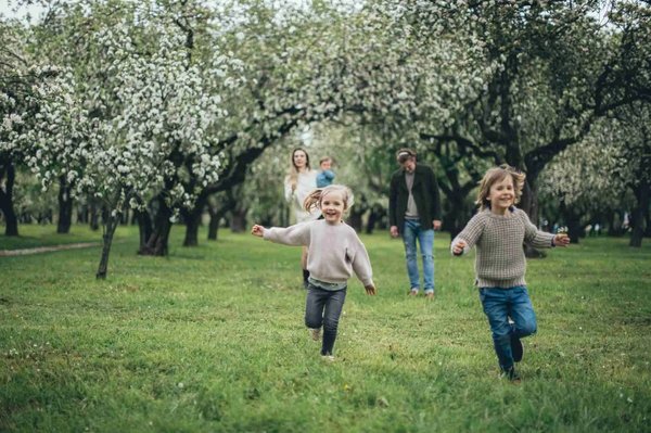 Bambini che corrono in un parco con alberi in fiore, atmosfera primaverile a Bologna.