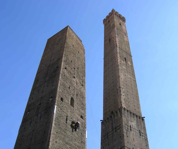 The Asinelli and Garisenda Towers in Bologna under a clear blue sky.