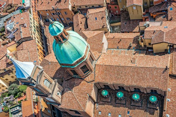 Aerial view of Bologna's terracotta rooftops with a green Baroque church dome.